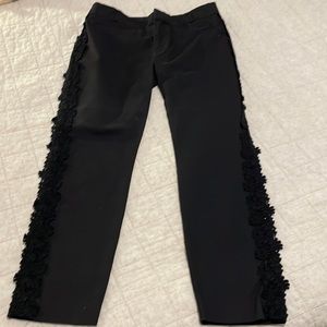 Anthropologie Black pants with lace flowers down sides.